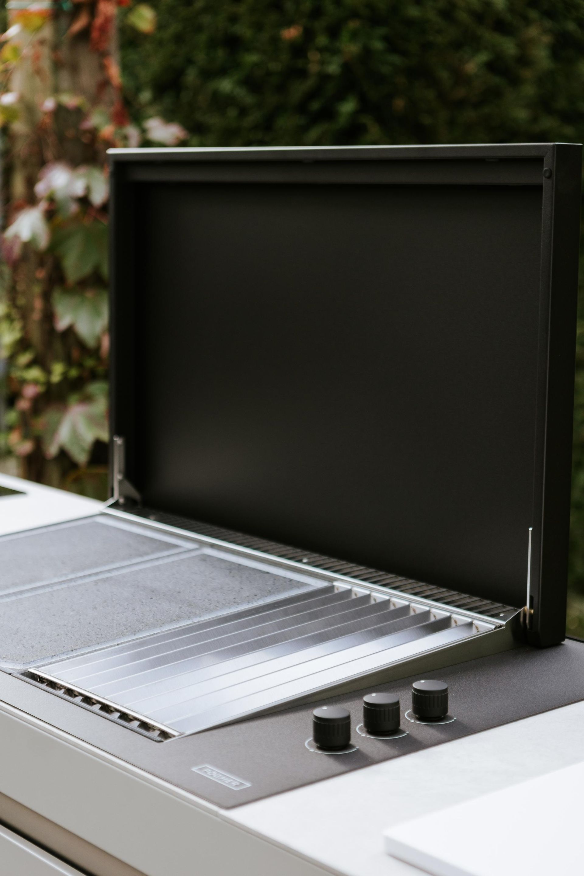 Griglia da esterno con coperchio aperto, metallo scuro, manopole di controllo.