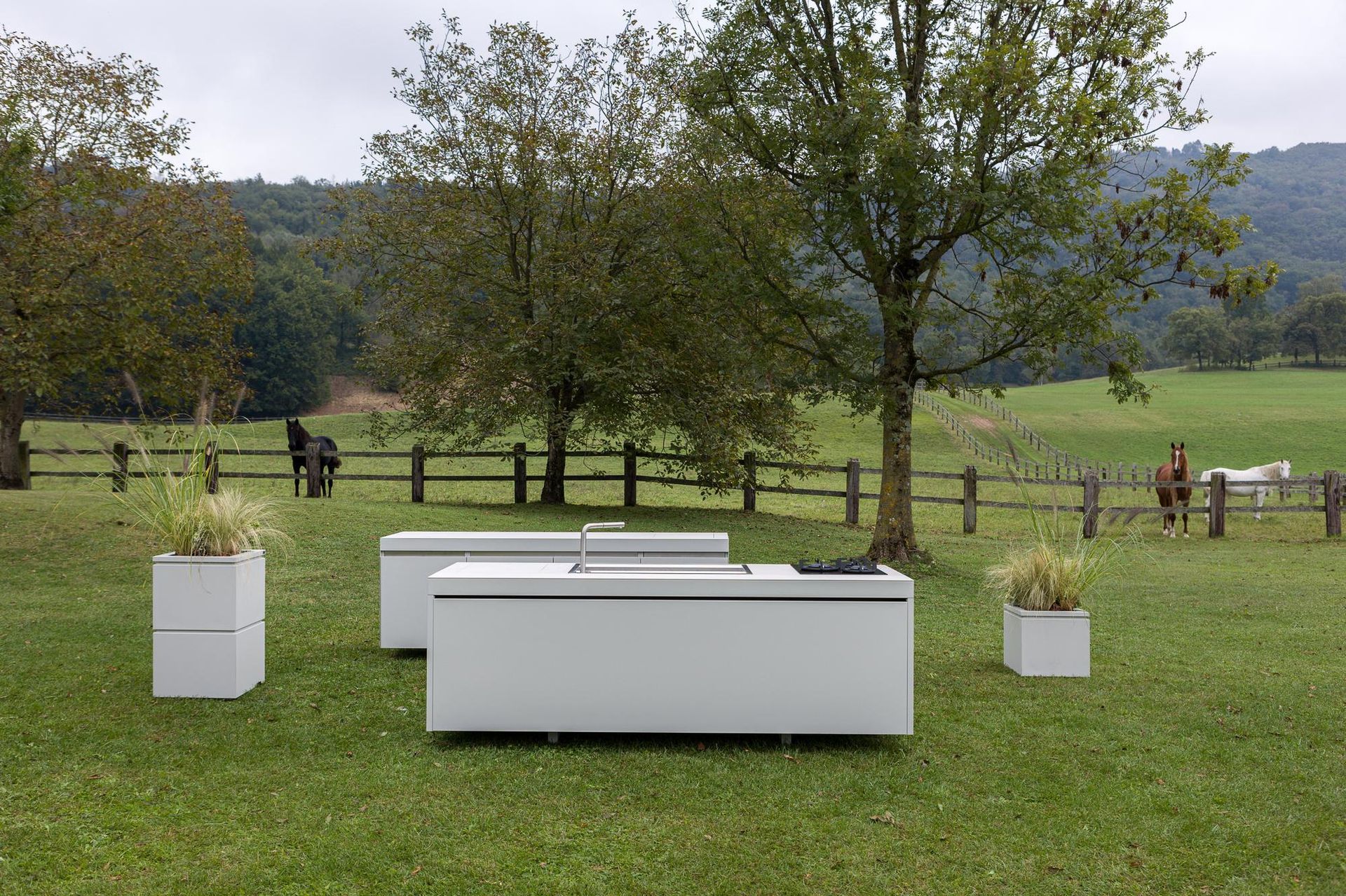 Cucina all'aperto situata in un campo erboso con cavalli sullo sfondo, sotto un cielo nuvoloso.