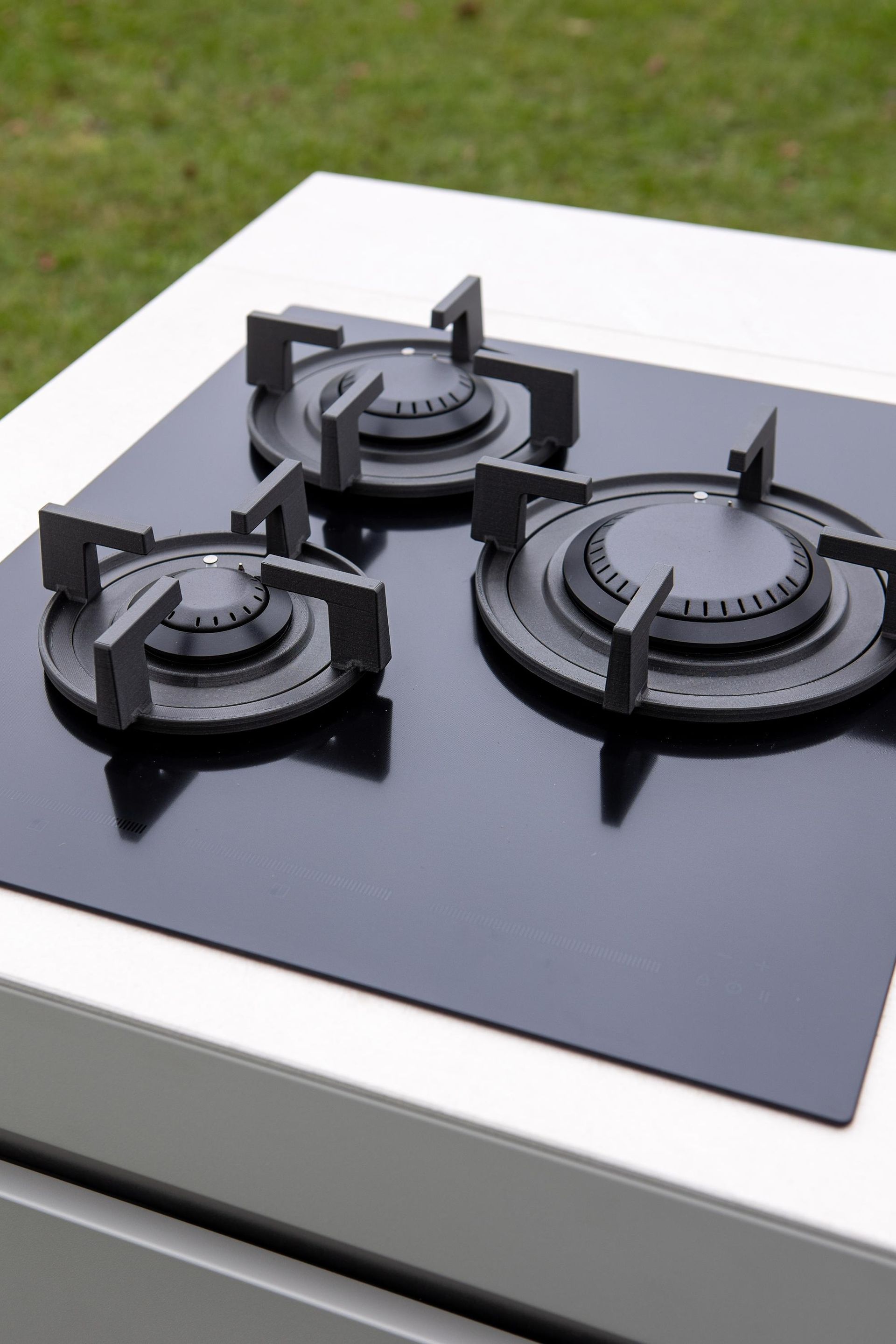 Piano cottura nero con tre fuochi a gas su un bancone bianco su uno sfondo verde sfocato.