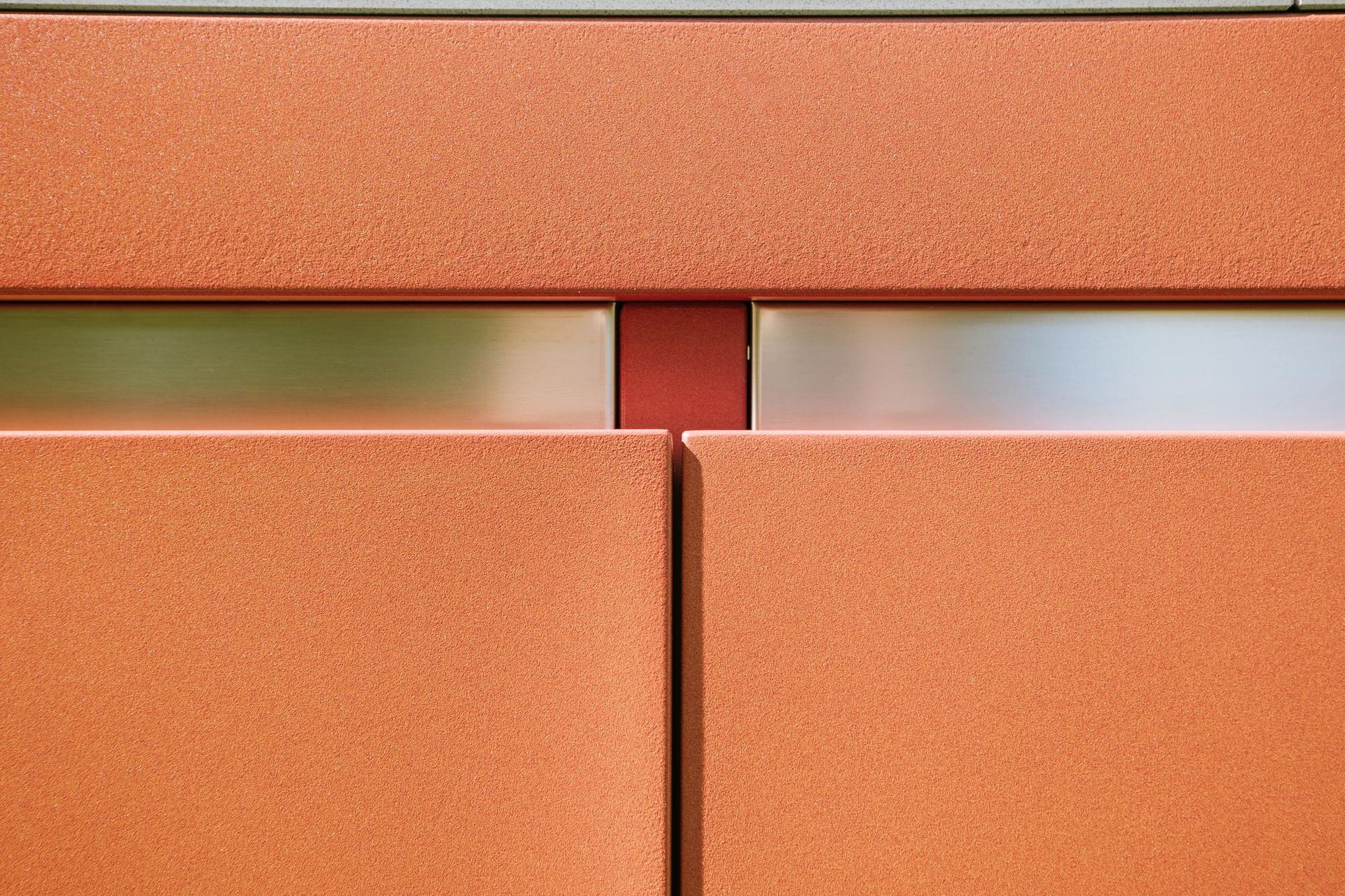 Muro di mattoni arancioni con accenti orizzontali argentati e rossi.