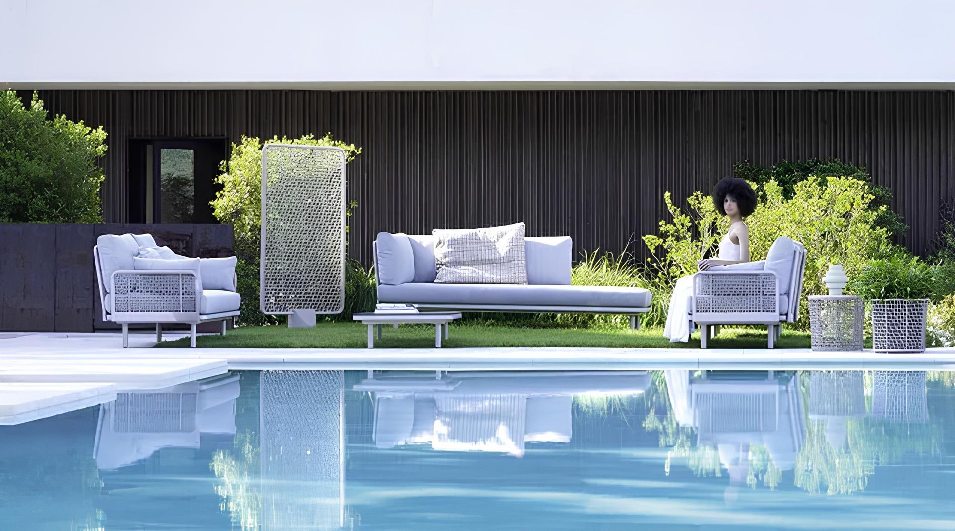 Mobili da giardino a bordo piscina. Cuscini azzurri, strutture in metallo e una donna.