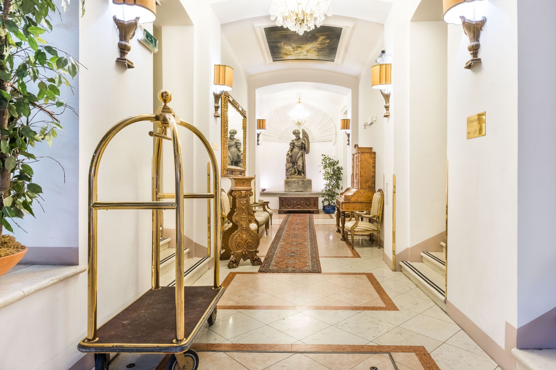 Hotel hallway with gold accents, ornate furniture, and a luggage cart.