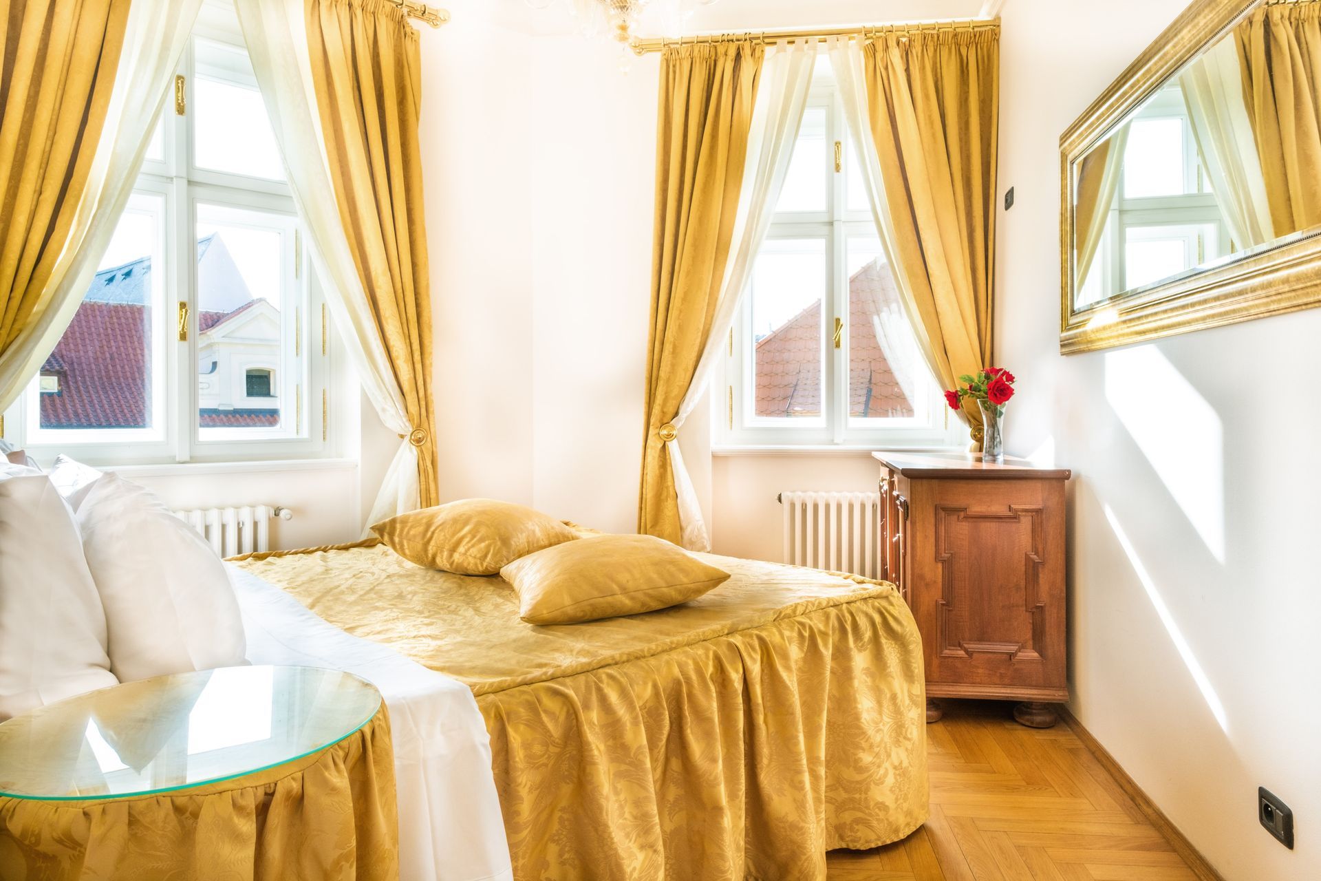Bedroom with golden decor, bed, two windows, wood floor, side table, and a mirror.