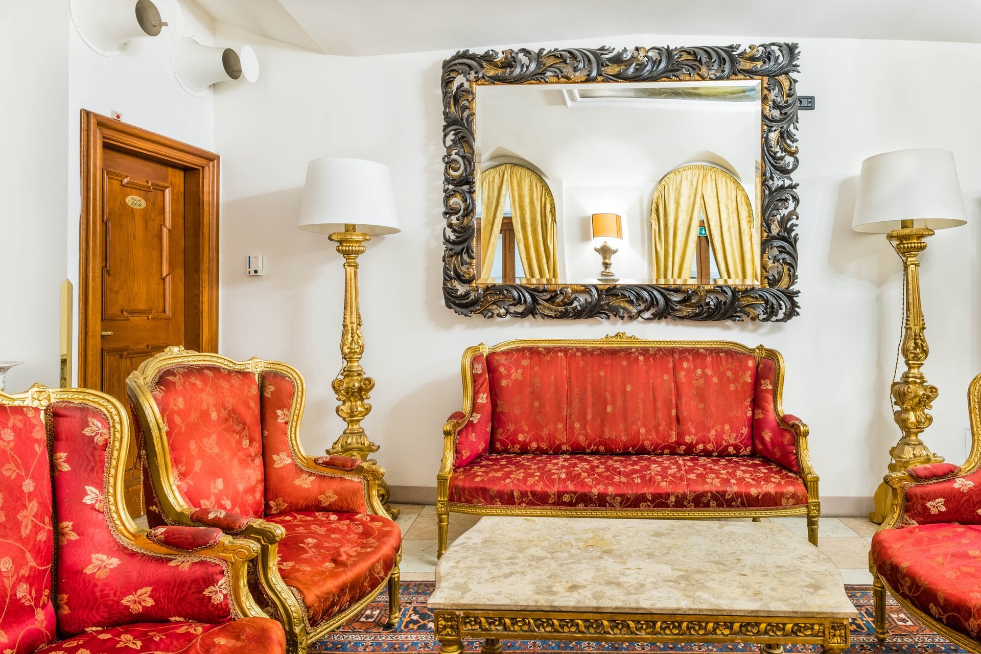 Ornate living room with red furniture, gold trim, large mirror, and gold lamps.