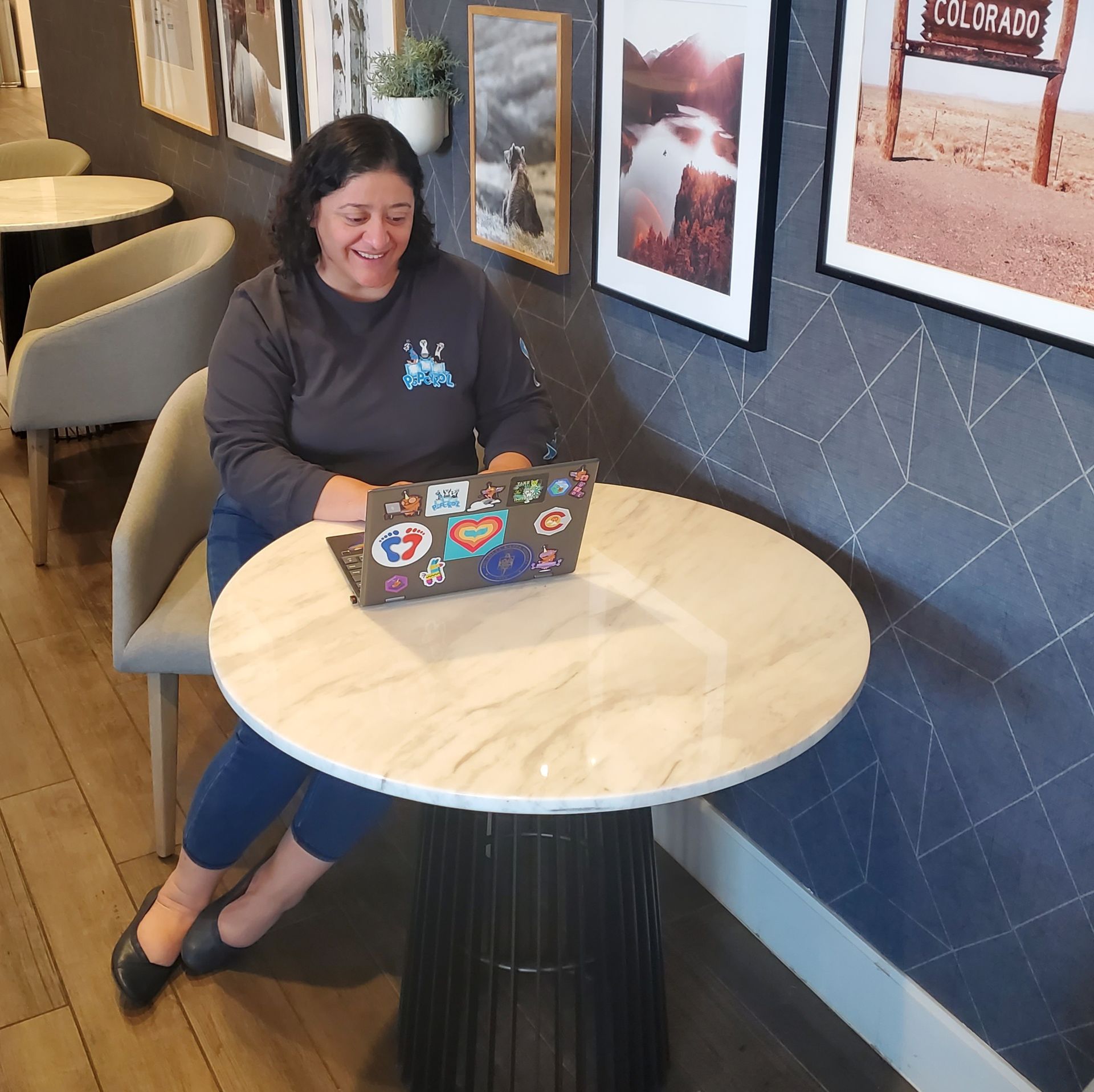 A woman is sitting at a desk with a laptop and a group of women are smiling.