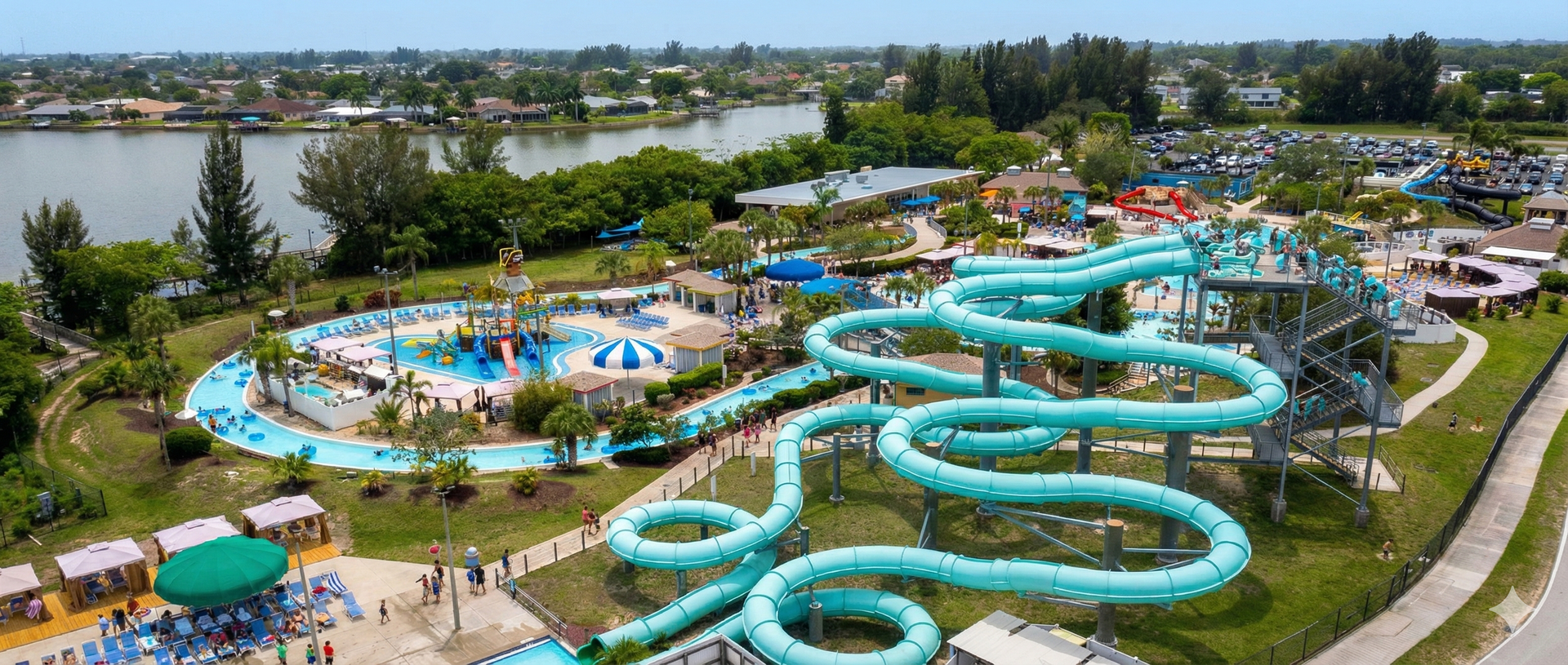 Aerial view of a water park with winding turquoise slides, pools, and a lake in the background.