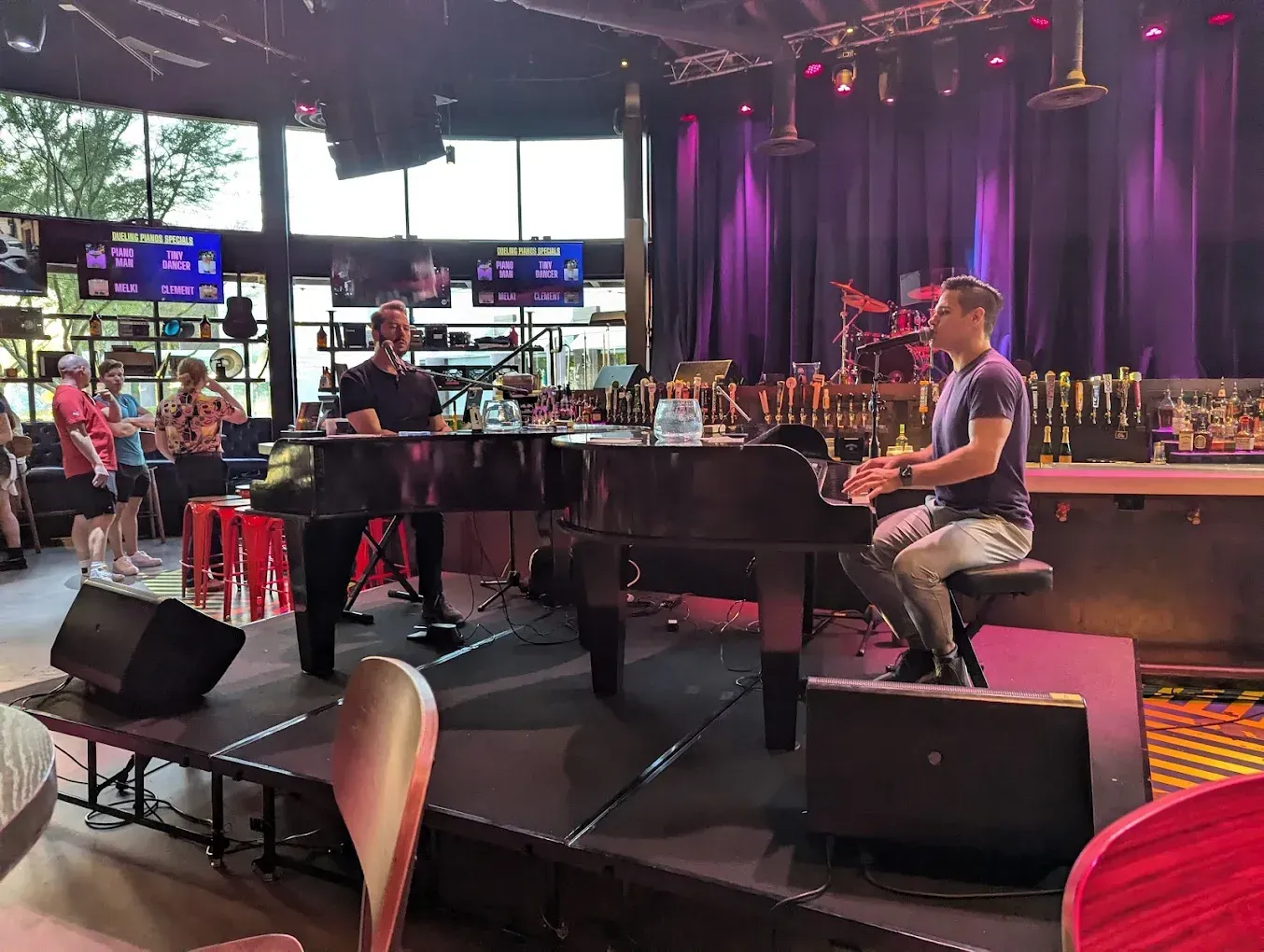 Waterfront shops with blue roofs at dusk. Boats docked, city in background.