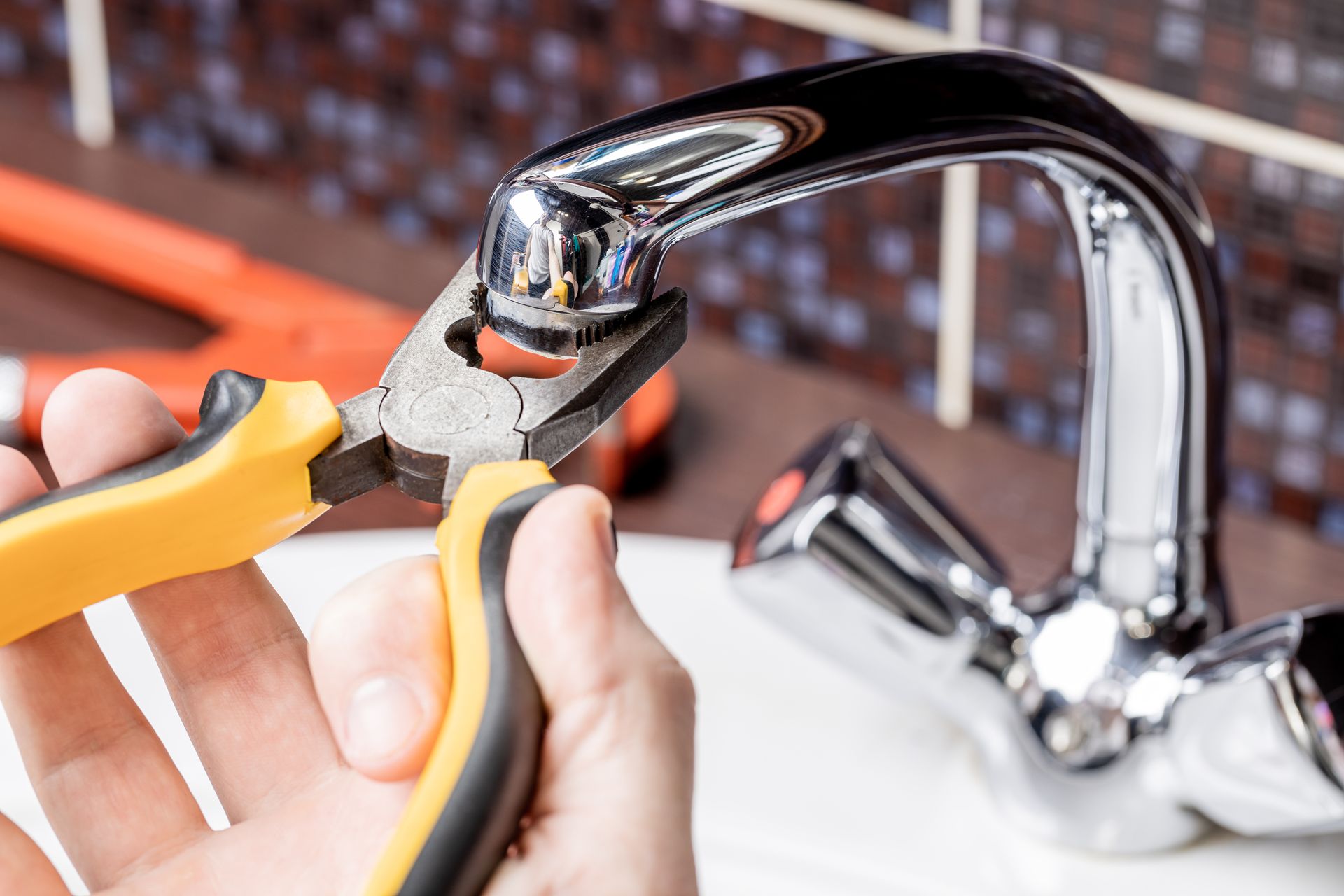Person using pliers to work on a chrome faucet in a bathroom.