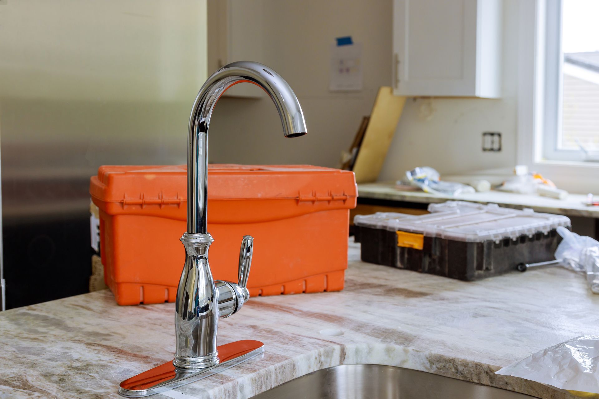 Silver kitchen faucet, orange toolbox, and tools on a marble countertop.