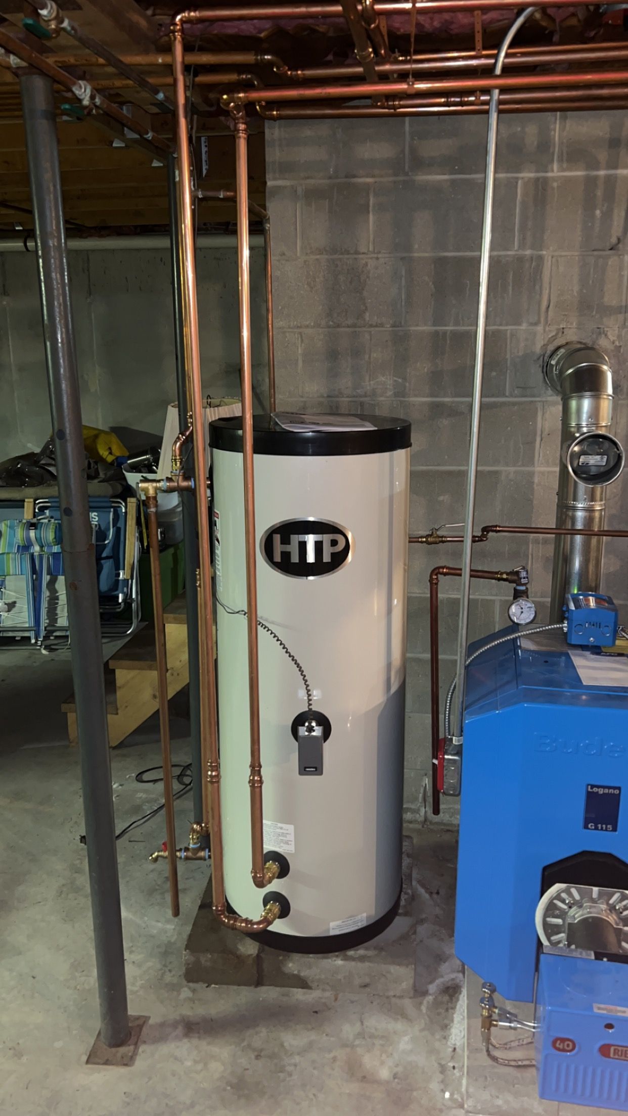 A water heater is sitting in a basement next to a blue boiler.