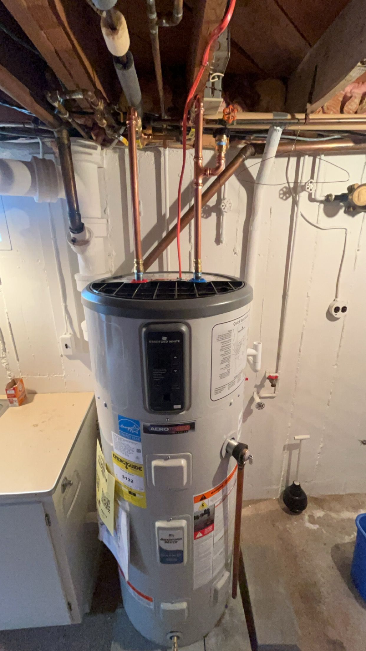 A water heater is hanging from the ceiling in a basement.