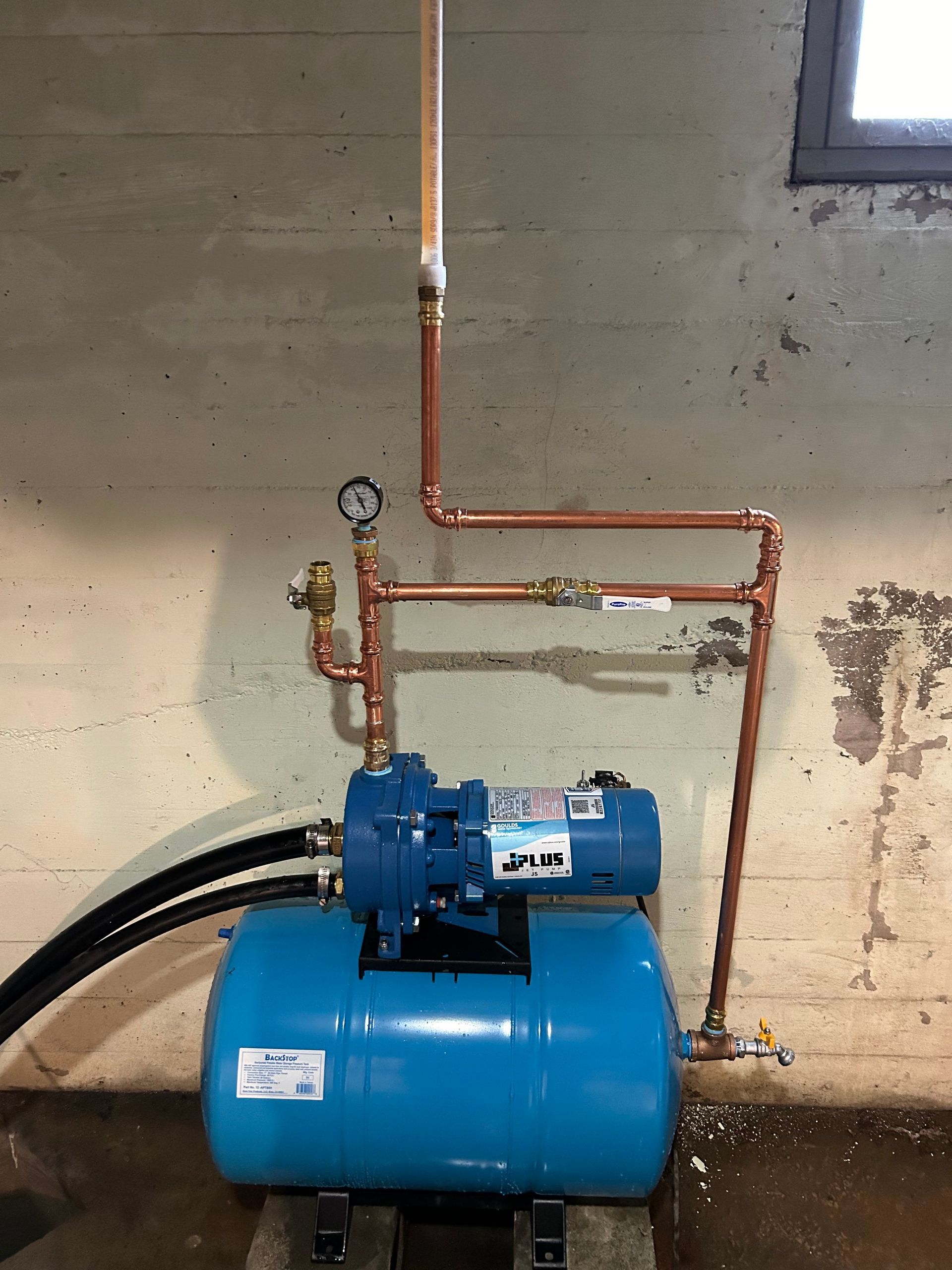 A blue water pump is connected to copper pipes in a basement.