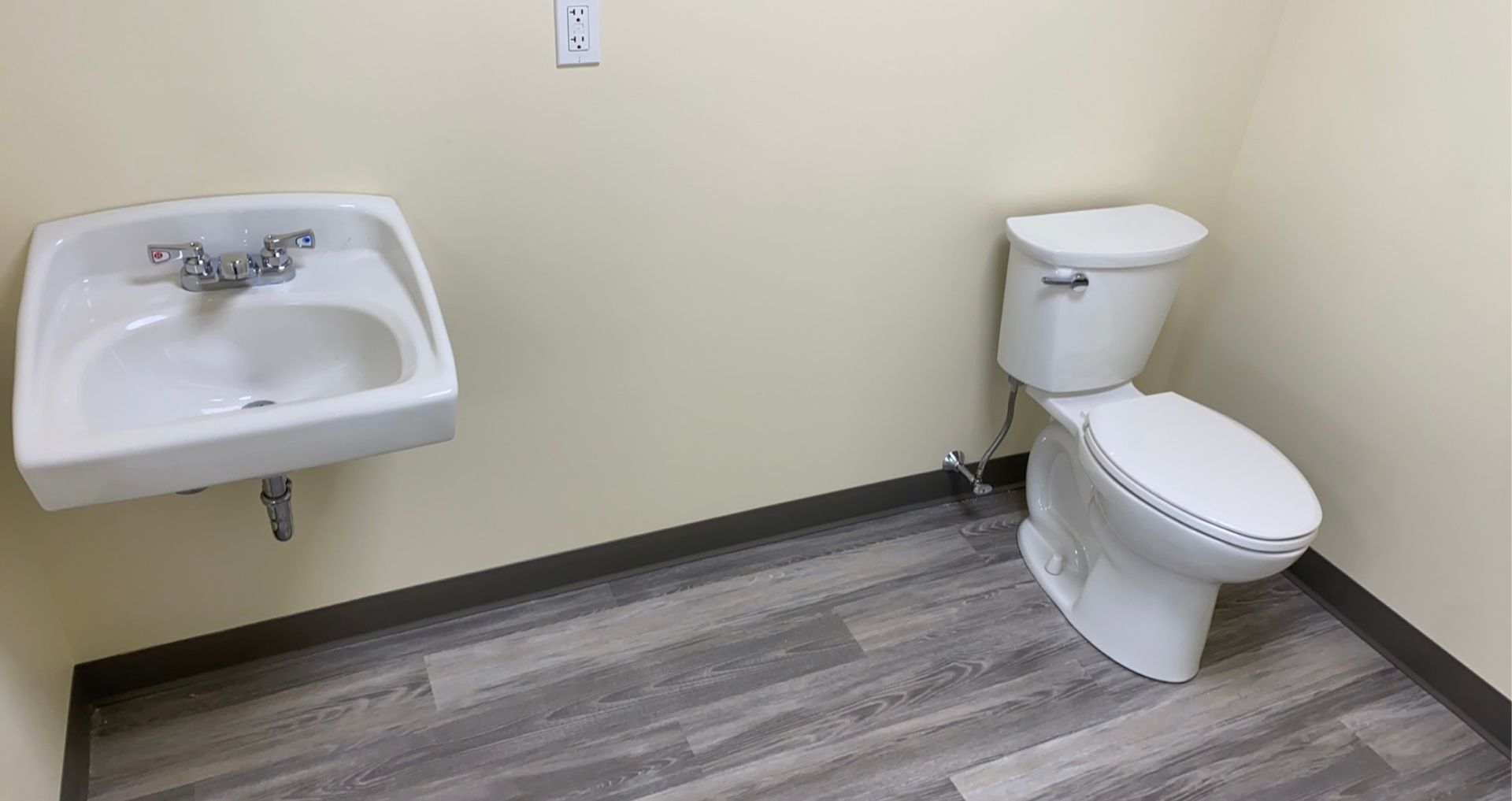 A bathroom with a toilet , sink and wooden floor.