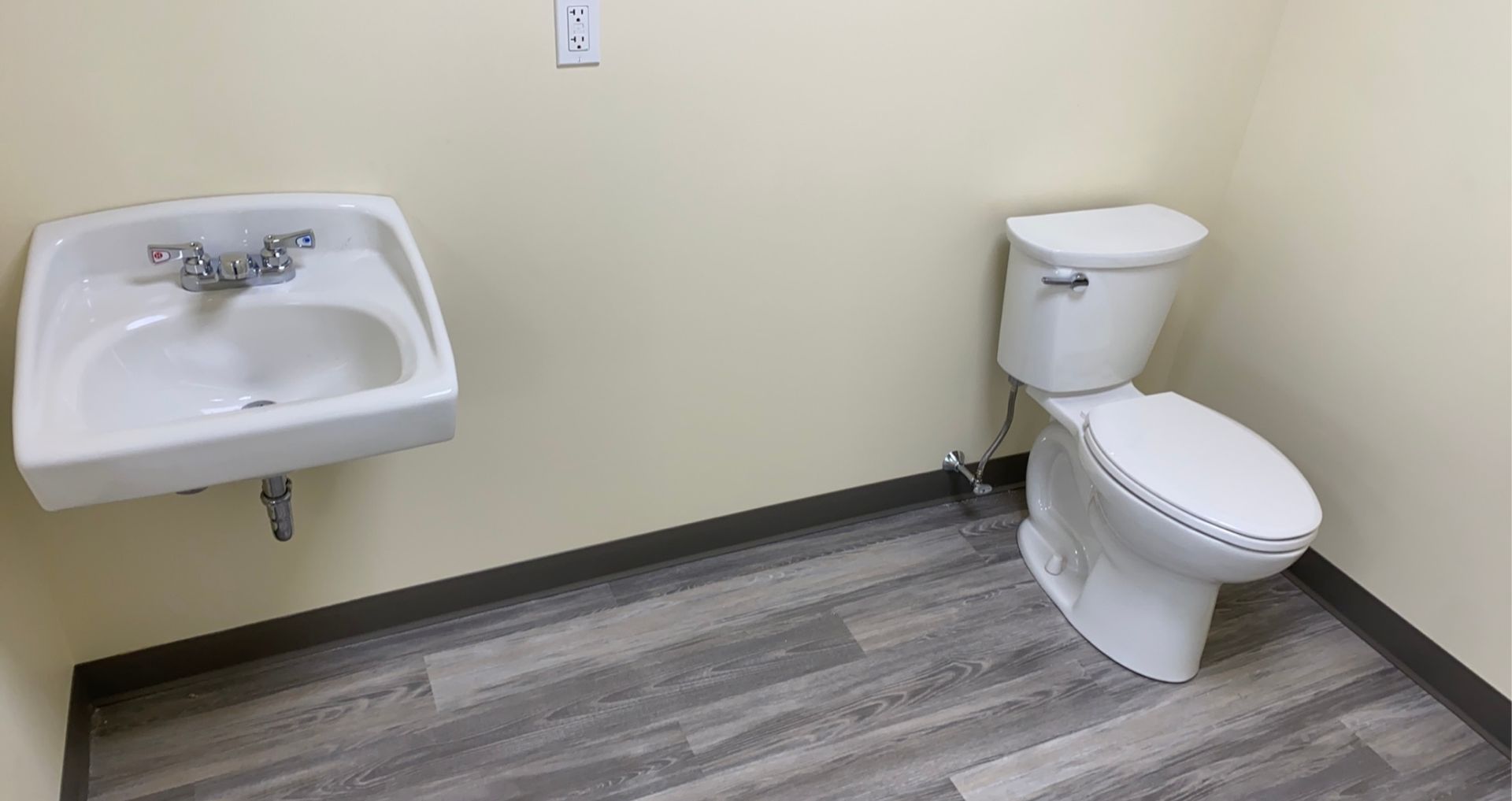 Small, empty bathroom with a white sink and toilet on a grey, wood-look floor.