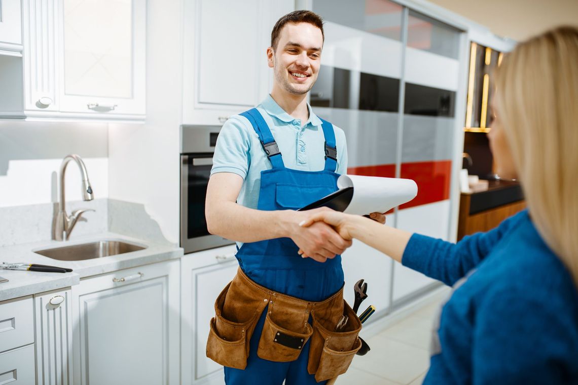 A man in overalls is shaking hands with a woman in a kitchen.