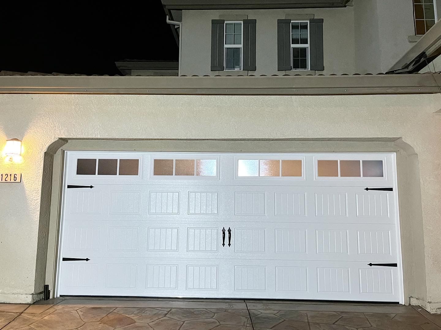 A white garage door is open in front of a house at night.
