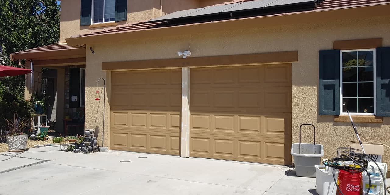 A house with two garage doors and a trash can in front of it