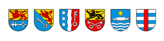 Sechs heraldische Schilde mit verschiedenen Symbolen, darunter Schlüssel, Sterne, Löwen und Wasser.