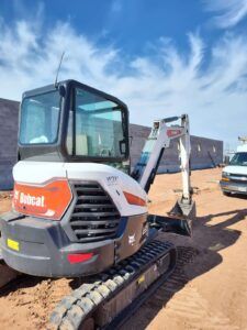 A bobcat excavator is parked in a dirt lot next to a van.