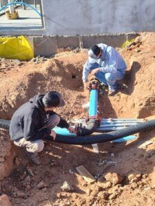 Two men are working on a pipe in the dirt