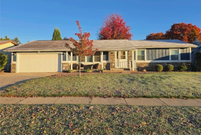 Ranch-style house with light siding and a beige garage door, surrounded by frosty grass and autumn foliage.