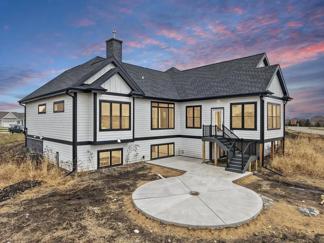 Two-story white house with black trim, dark roof, concrete patio, and cloudy sunset.