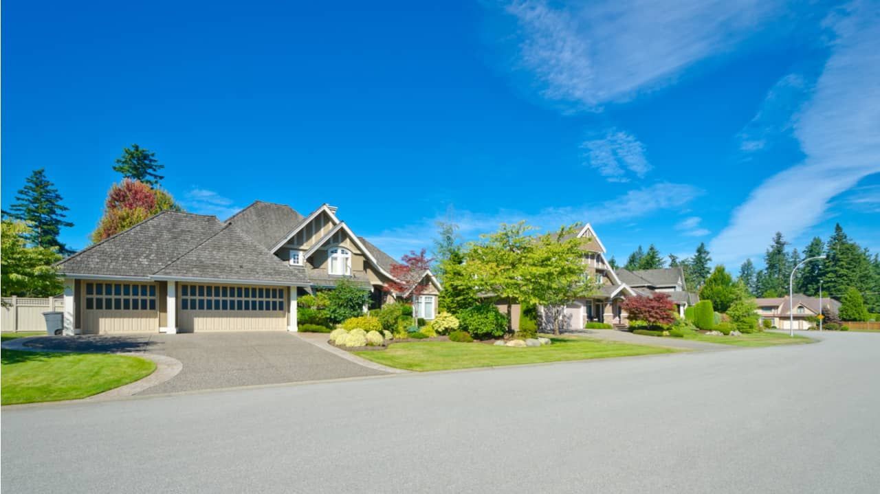 Houses on a sunny day with blue sky and green trees. Driveways and lawns in front.