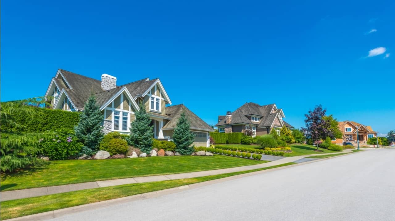 Houses with green lawns and blue sky along a sunny street.