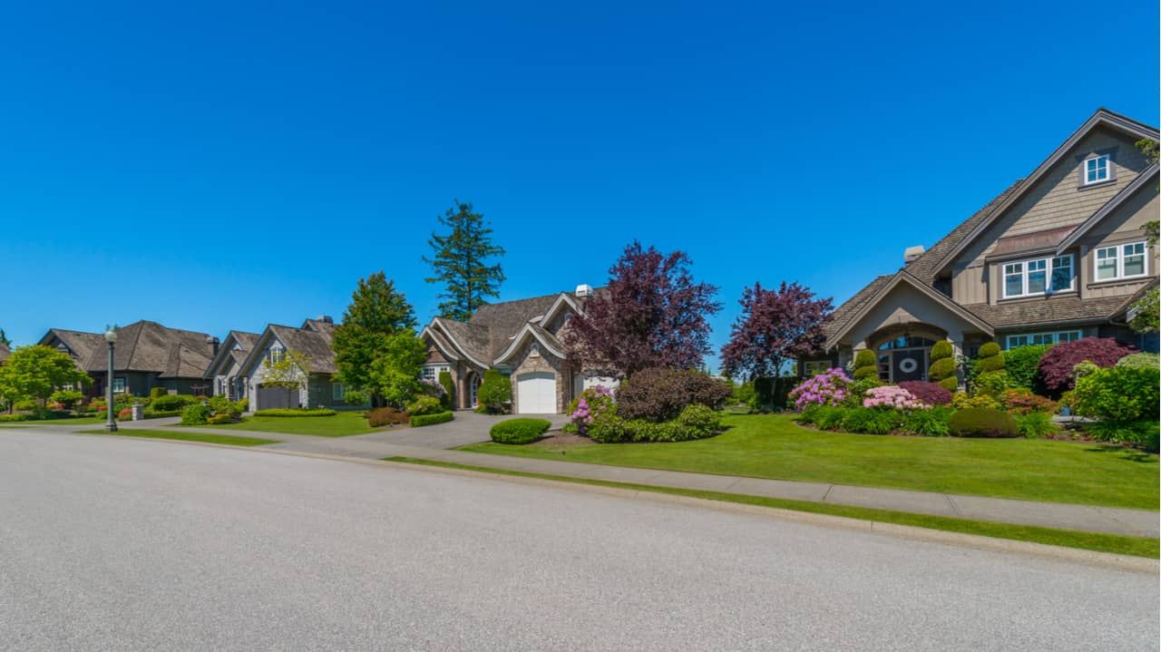 Row of houses with green lawns and colorful landscaping under a clear blue sky.
