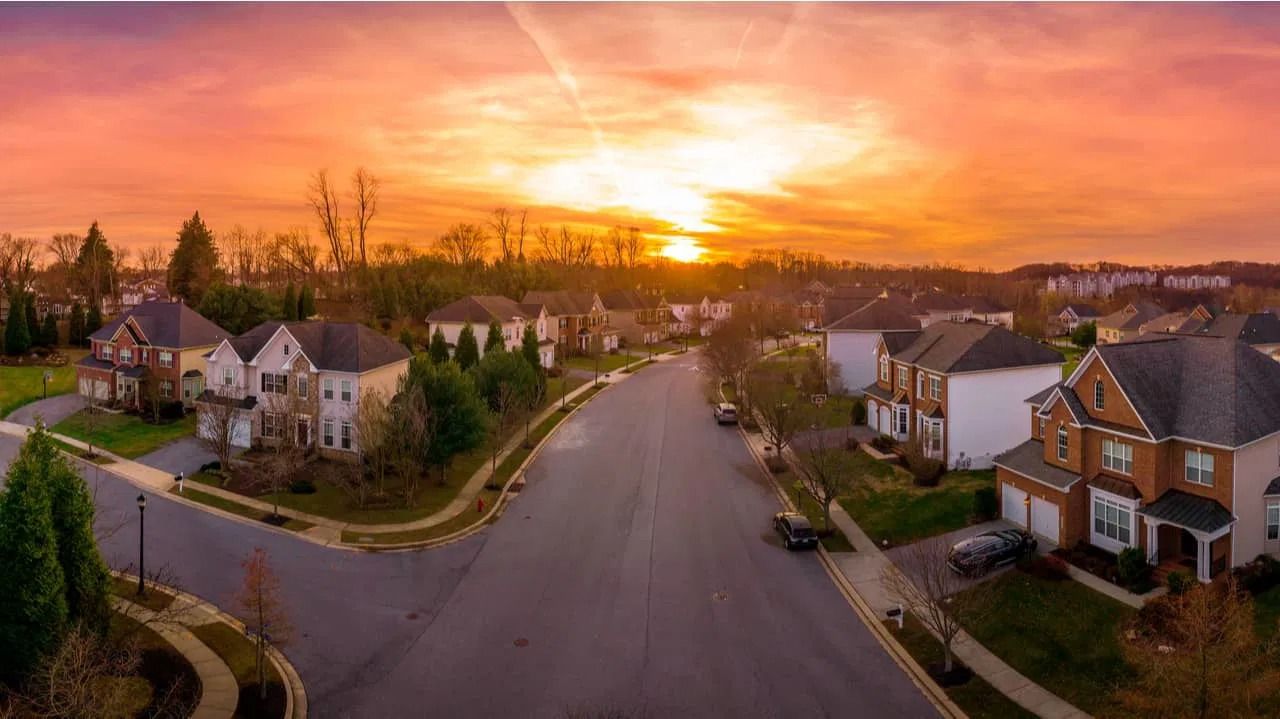 Suburban street at sunset with houses and vibrant orange and yellow sky.