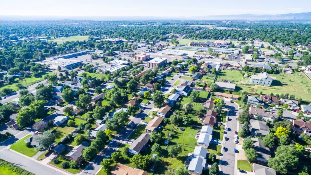 Aerial view of a suburban neighborhood with houses, trees, and buildings under a clear sky.