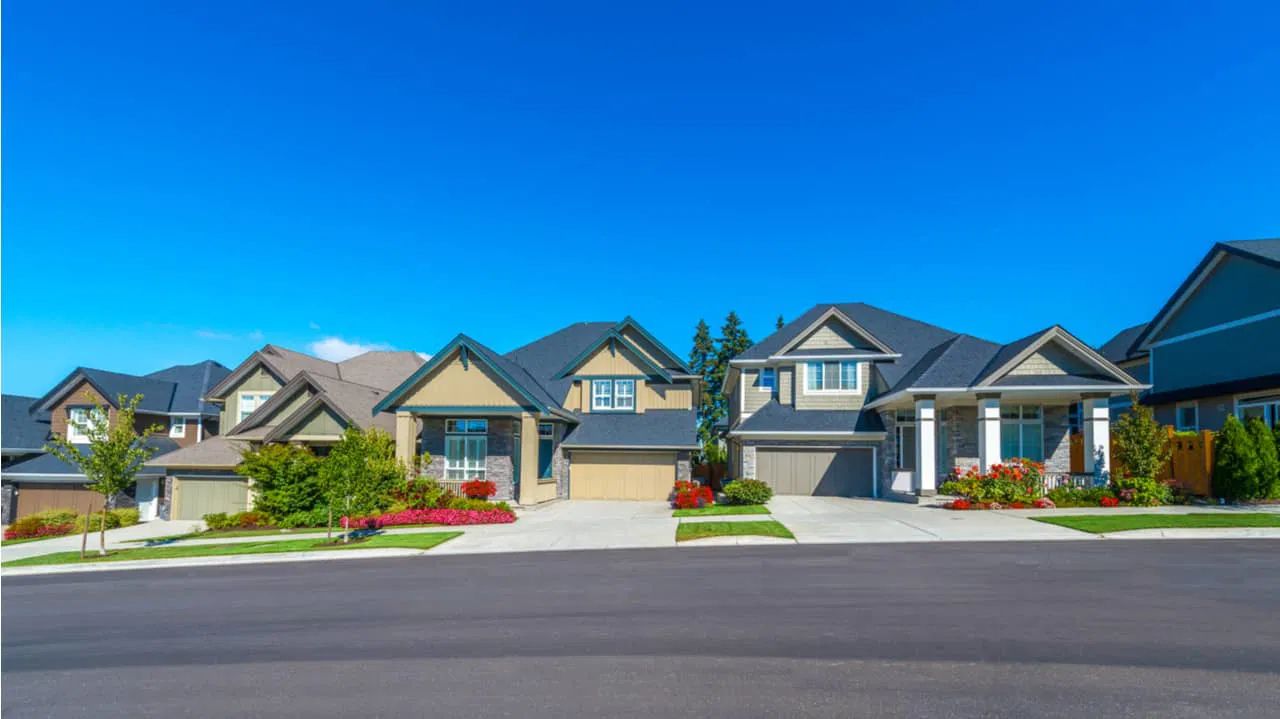 Row of houses with driveways, on a street under a bright blue sky.