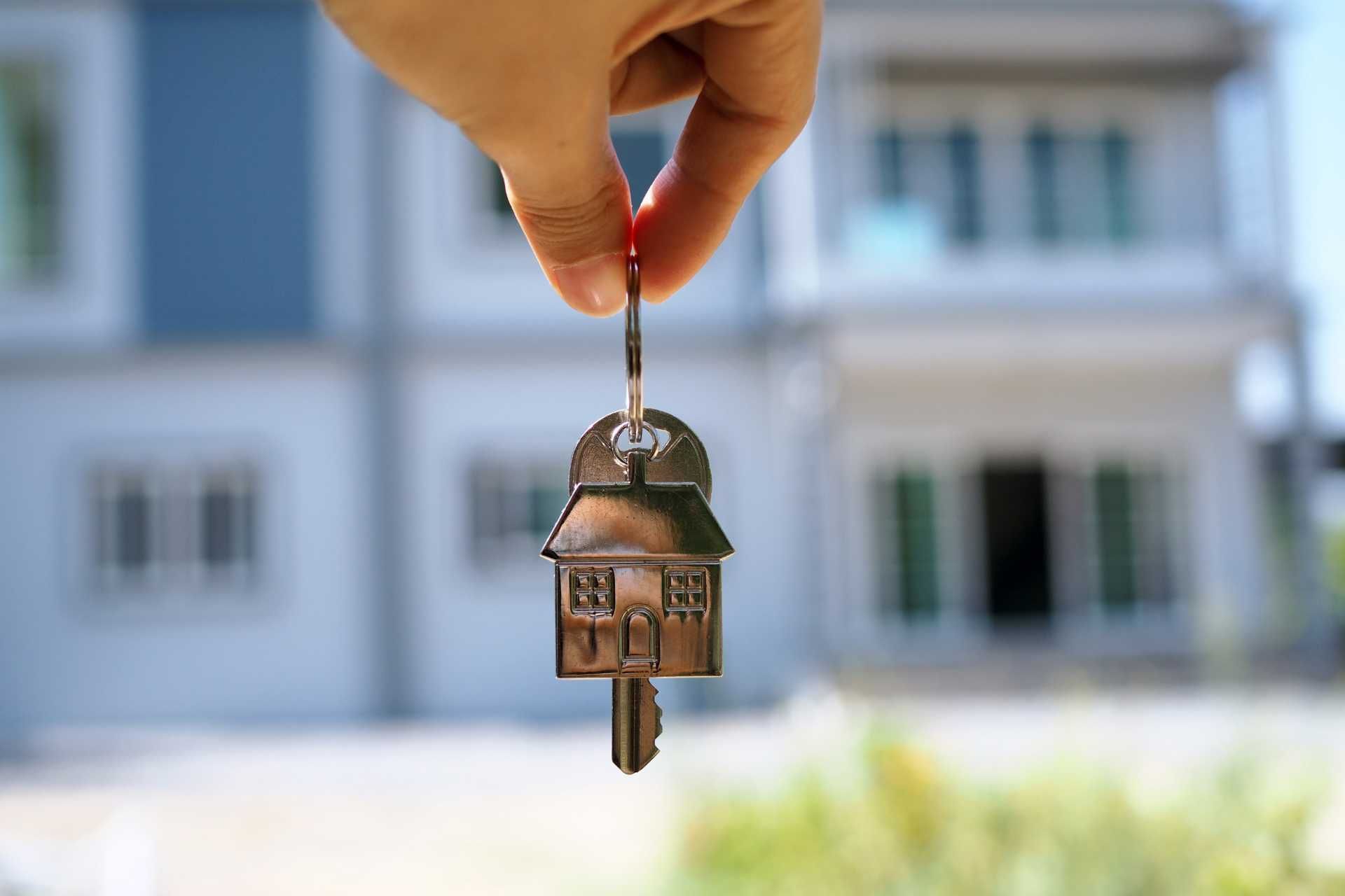Hand holding house key with home in the background.