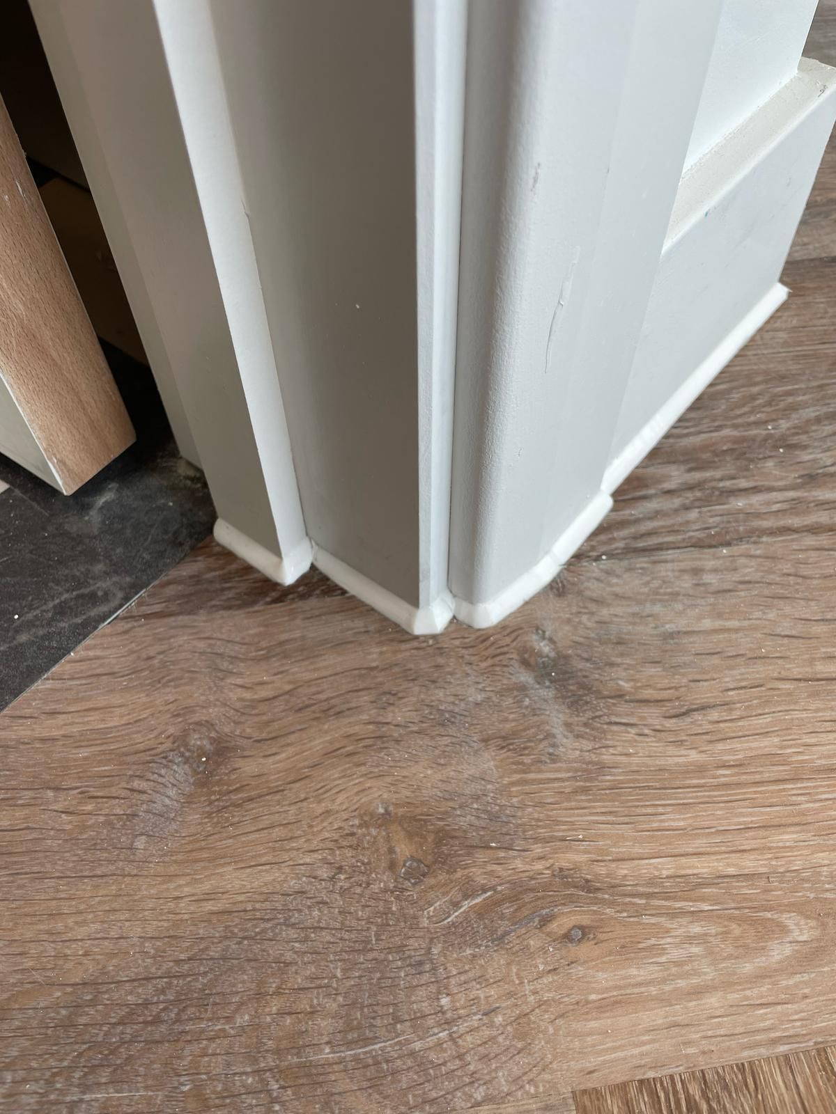 White door frame corner with base molding, brown wood-look flooring.
