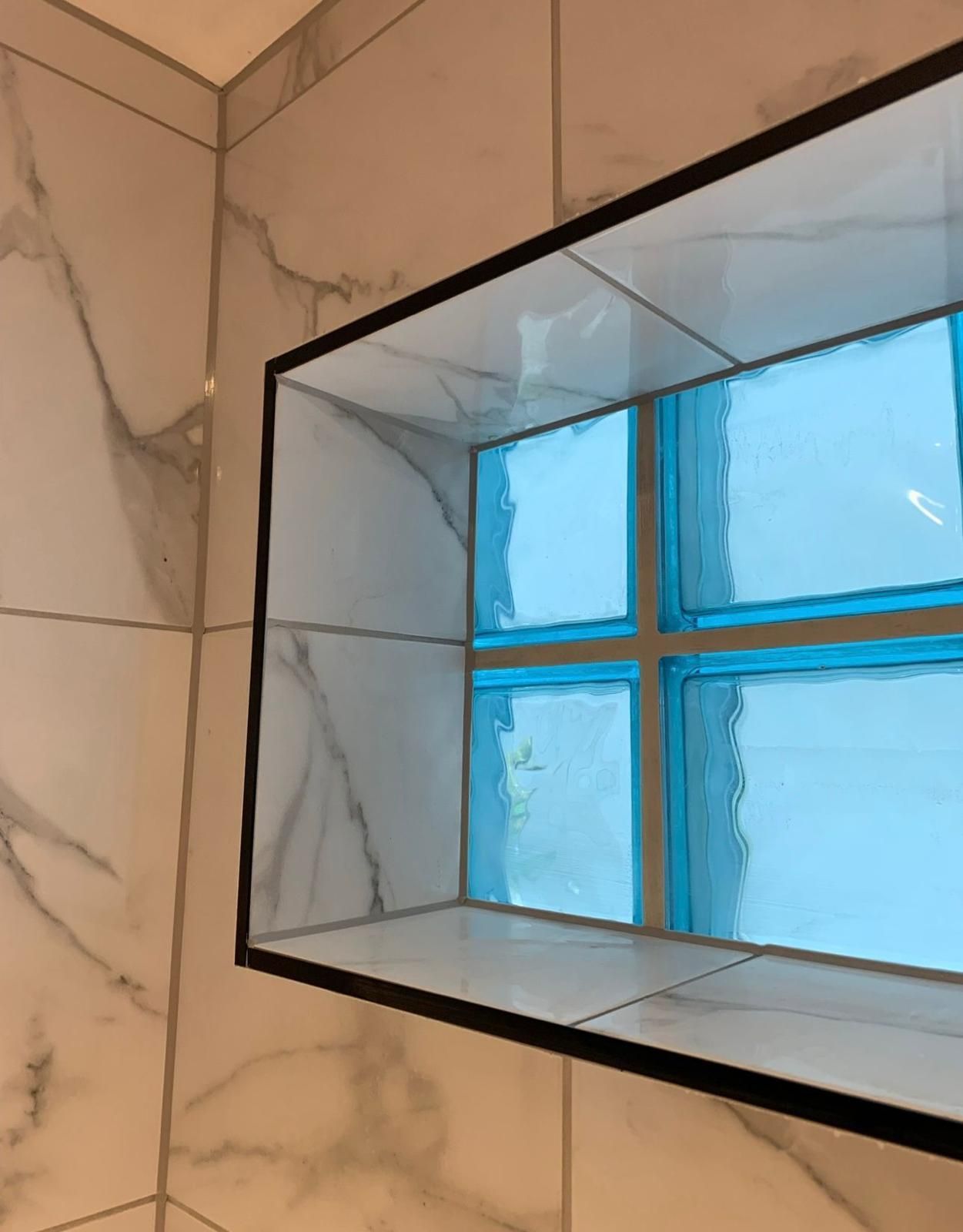 Niche in a tiled shower with a window of blue textured glass, framed in black.