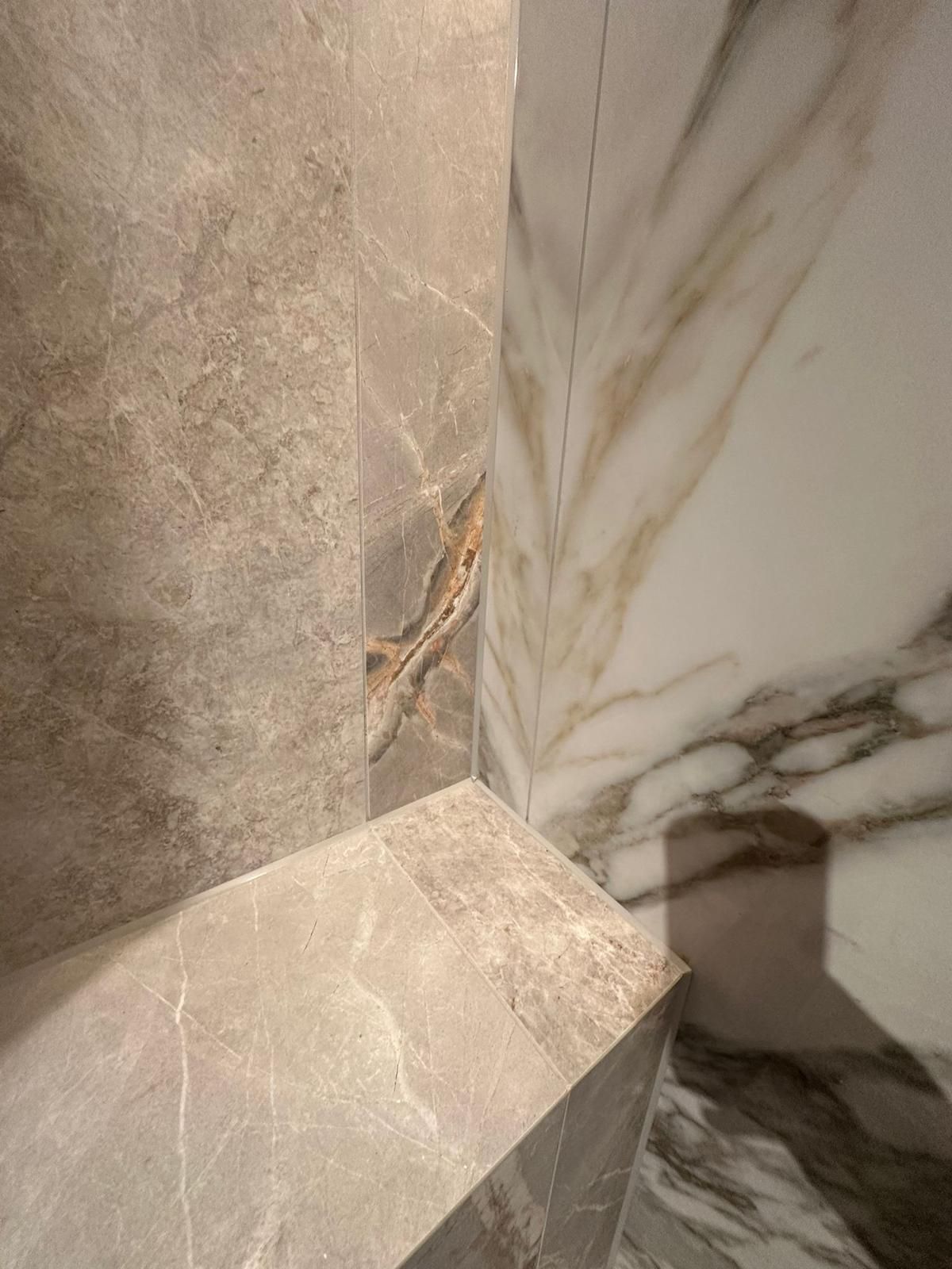 Corner of a modern bathroom featuring marble-like tiled surfaces in shades of gray, beige, and white.