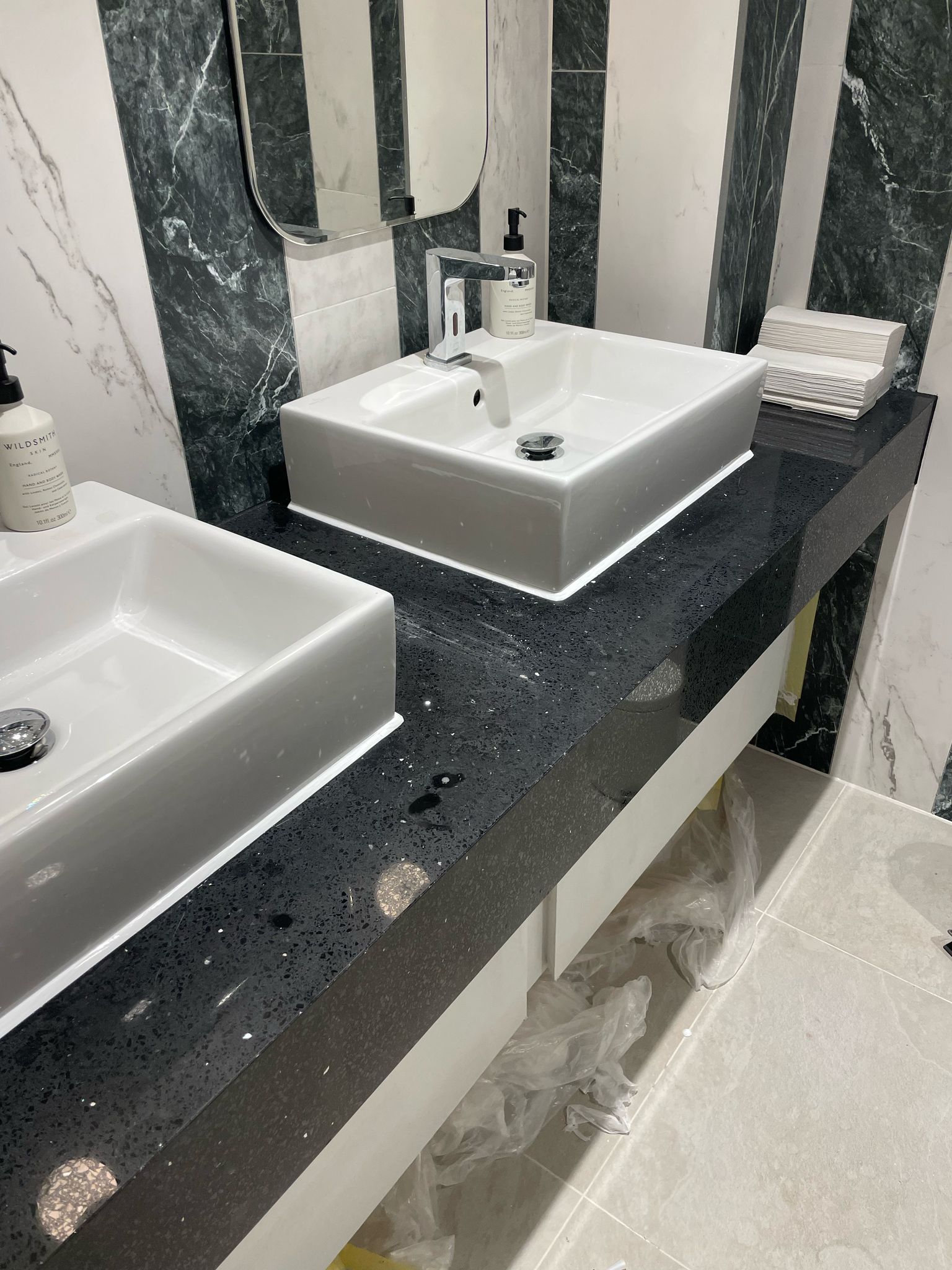 Bathroom with two white rectangular sinks on a dark speckled countertop. Striped walls.