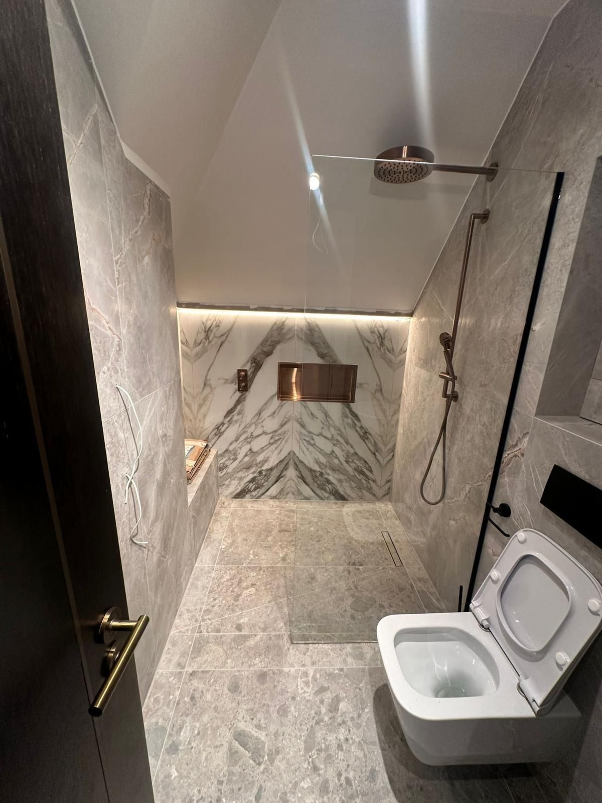 Modern bathroom with gray marble tiles, shower, toilet, and gold fixtures.