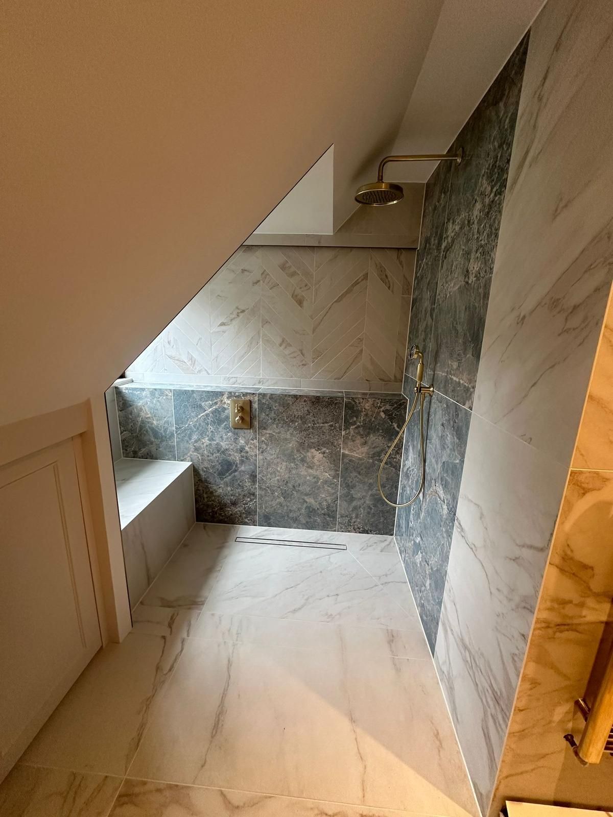 Bathroom with marble tile, angled ceiling, showerhead, and built-in bench.