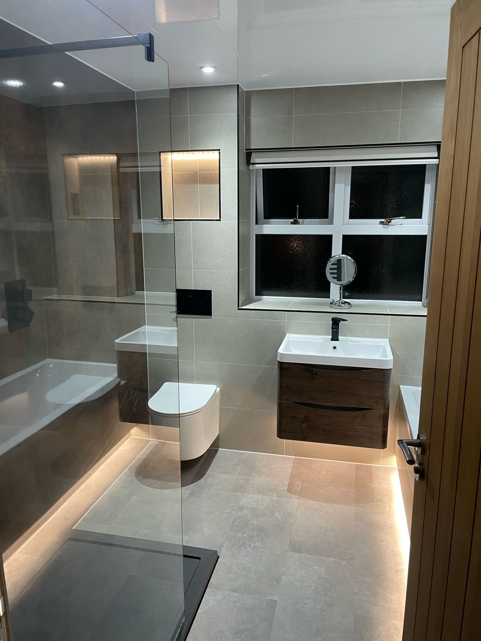 Modern bathroom with a bathtub, toilet, sink, and window. Soft lighting and neutral tones.