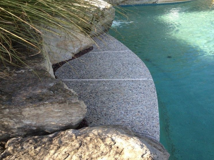 A swimming pool surrounded by rocks and grass with a staircase leading to it.
