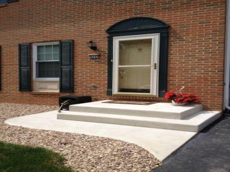 A brick house with a concrete porch and steps leading to the front door.