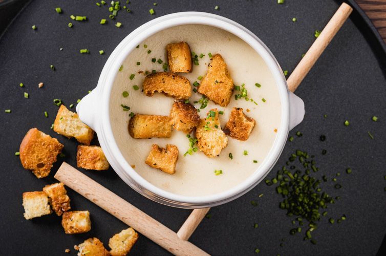 Eine Schüssel Suppe mit Croutons obendrauf auf einem schwarzen Teller.