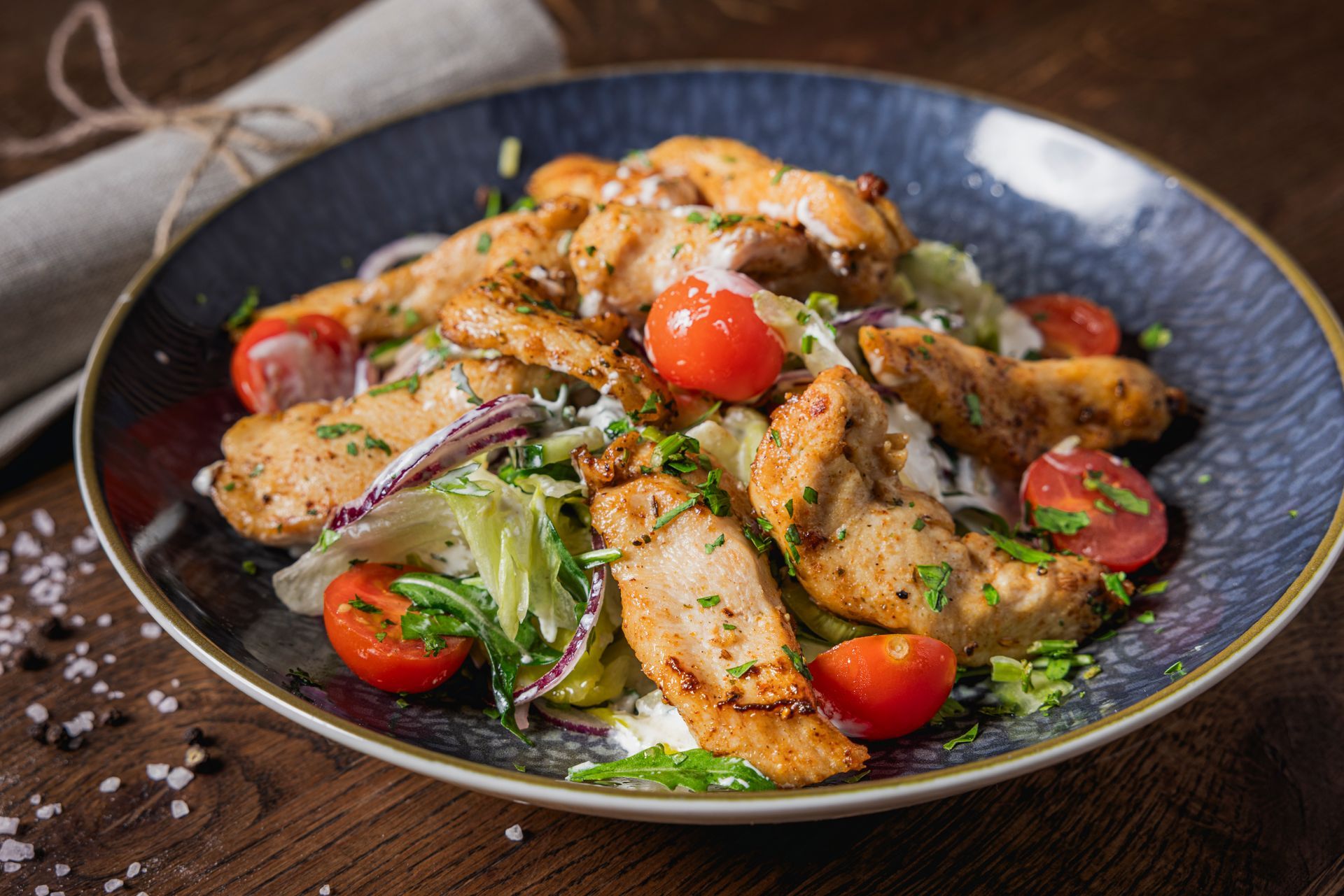 Ein Teller Hühnersalat mit Tomaten und Salat auf einem Holztisch.