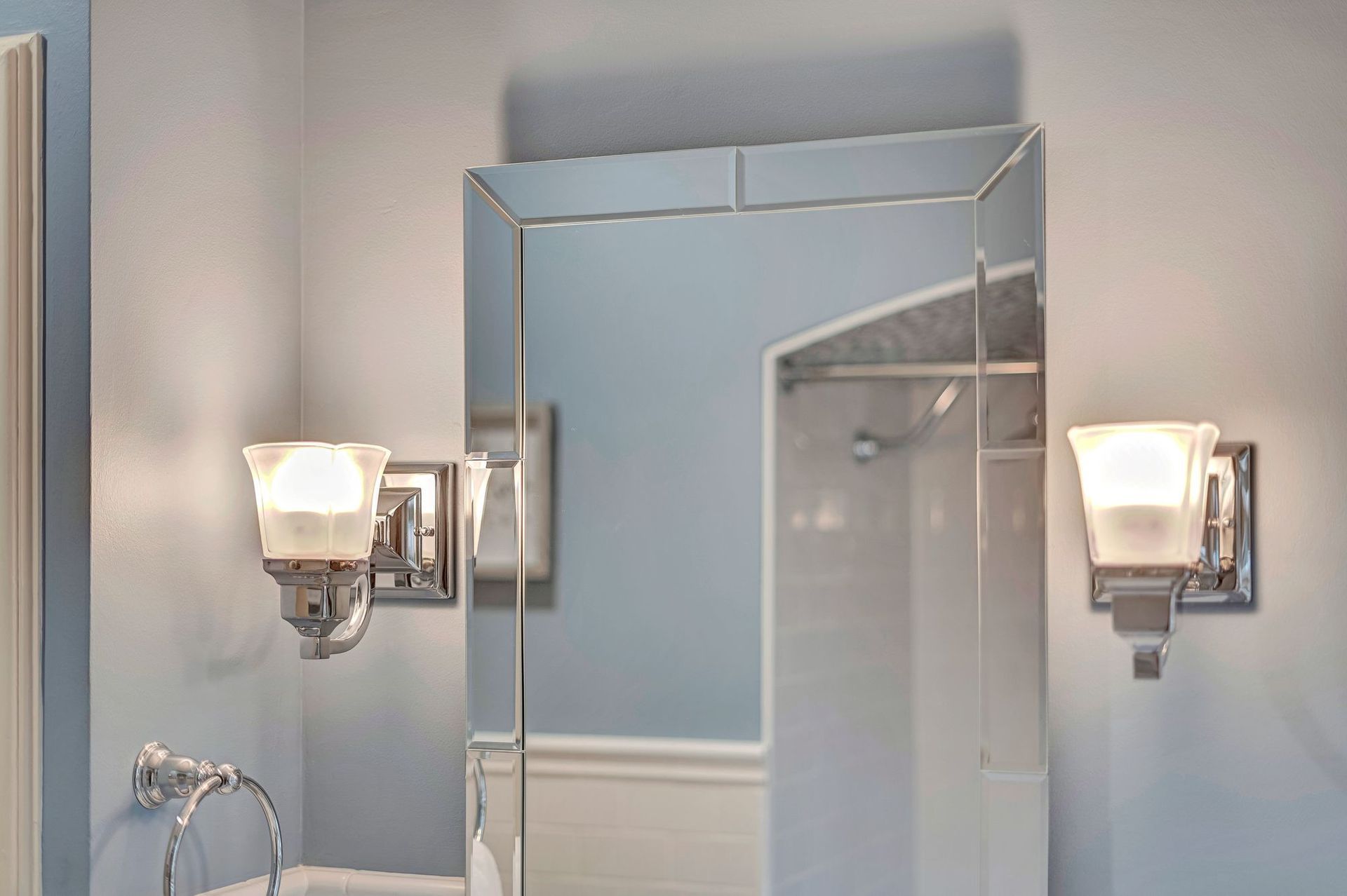 Bathroom mirror with two sconces; blue walls, white trim, and a glimpse of a shower.