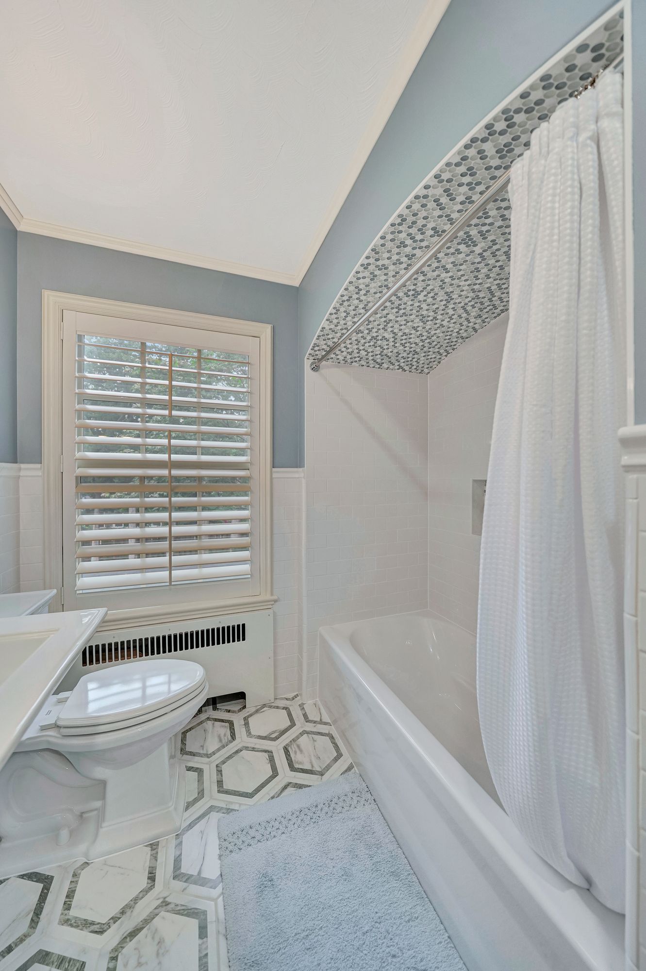 Bathroom with blue walls, white fixtures, hexagonal patterned floor, and shower curtain.