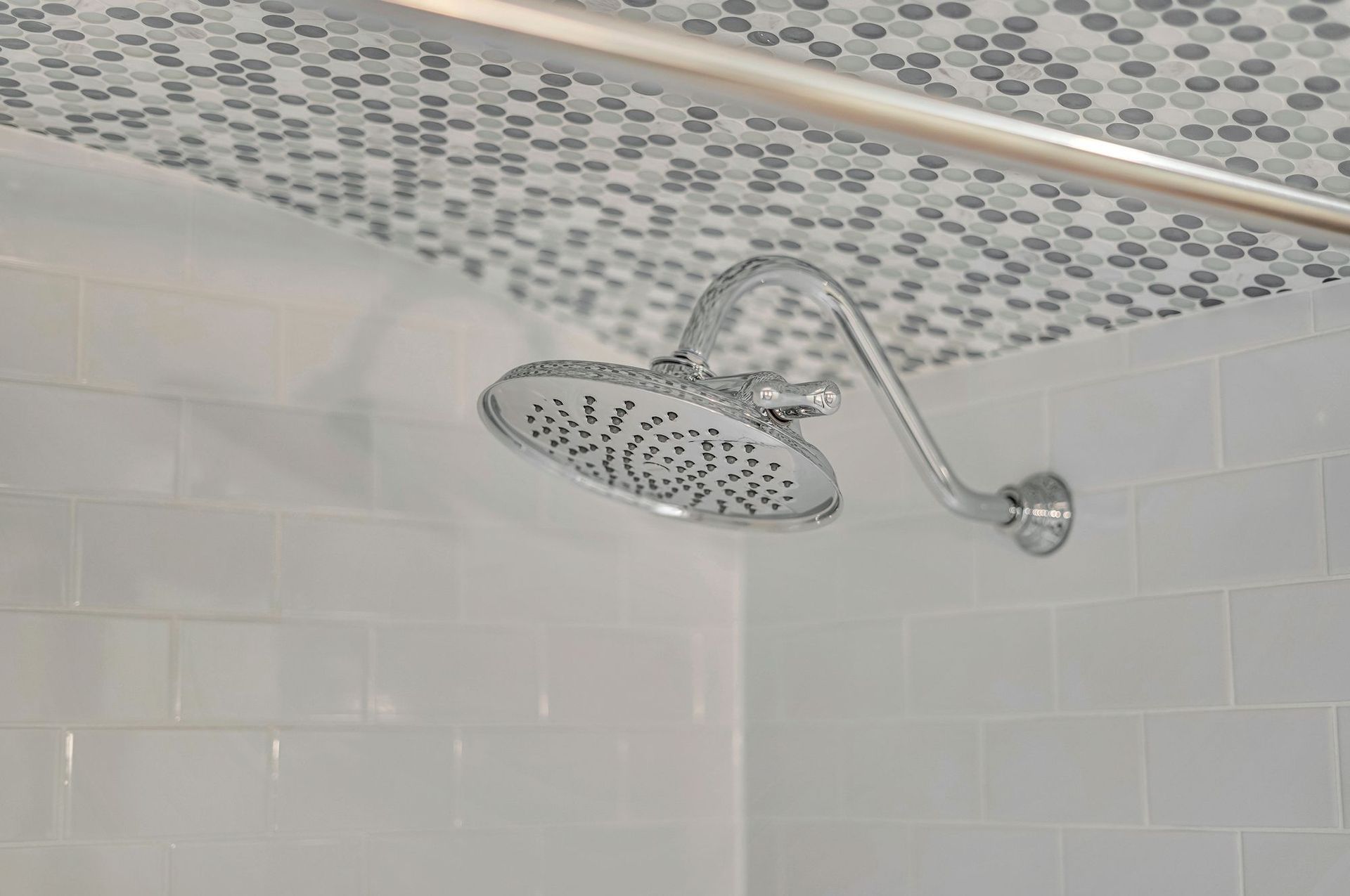 Chrome shower head in a tiled shower with a patterned ceiling.