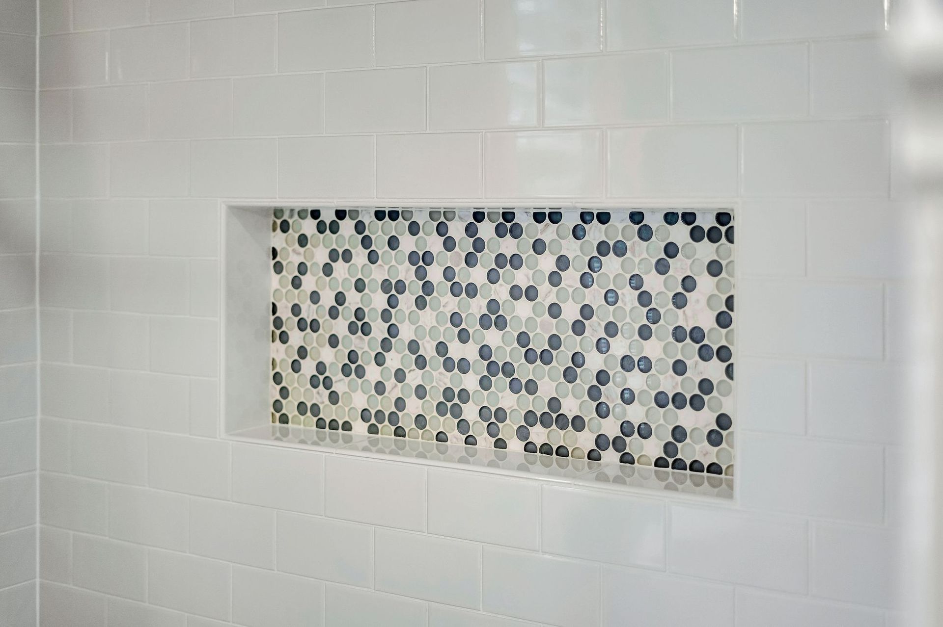 White tiled shower wall with recessed shelf featuring mosaic tile.