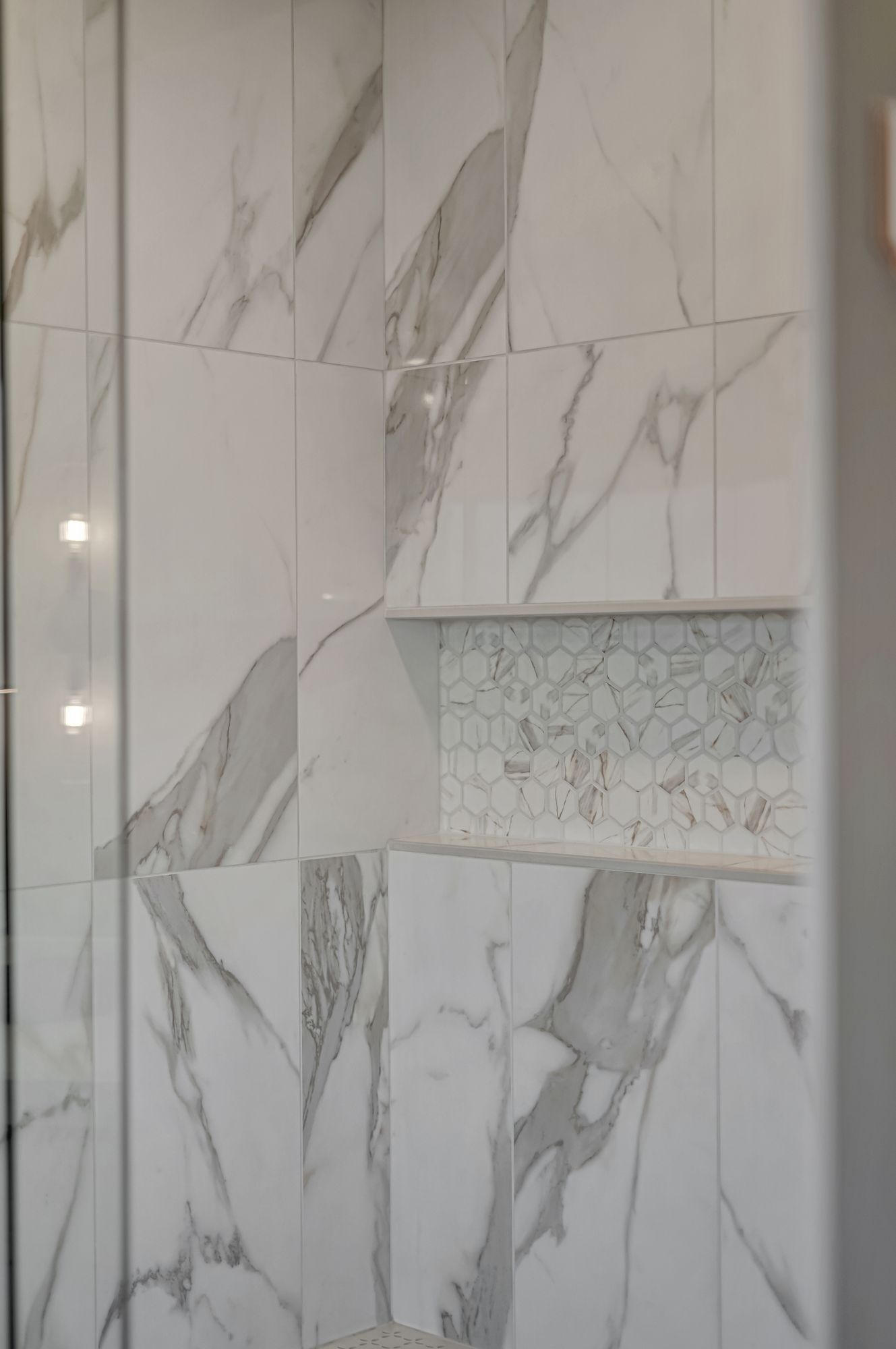 White marble-tiled shower with a built-in shelf lined with mosaic tiles.