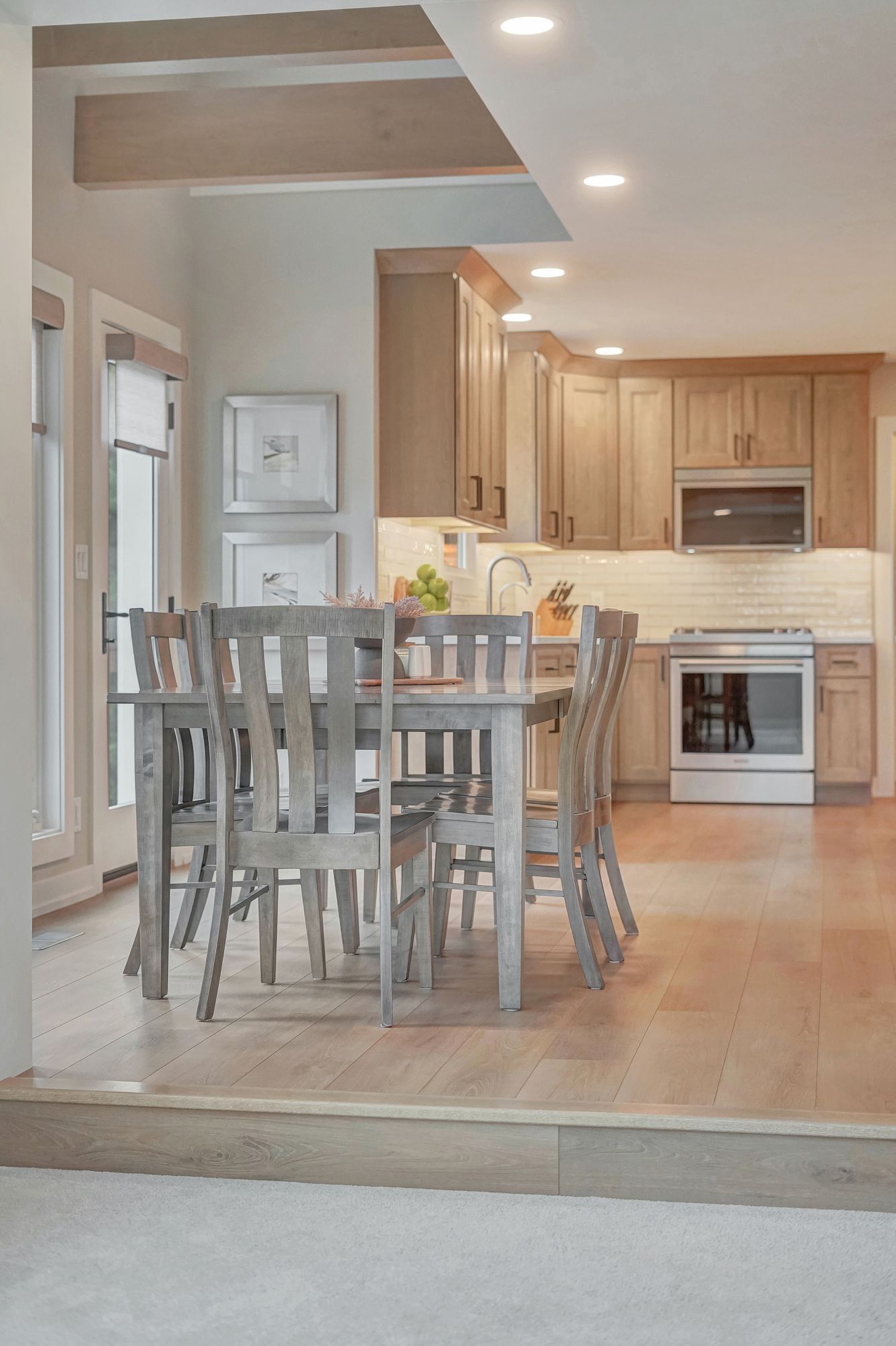 Dining area and kitchen with wooden table, chairs, cabinets, and appliances. Bright lighting and neutral colors.